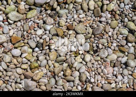 Il sole splende su piccole pietre di ghiaia alla spiaggia di Limni a Corfù, Grecia - il mare è cristallino qui - le rocce nella foto sono in realtà sotto acque poco profonde Foto Stock