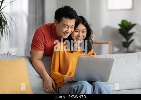 Uomo e donna asiatici che guardano lo schermo del notebook, gli interni della casa Foto Stock