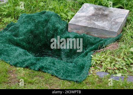 piccola tomba aperta coperta da un tappeto verde prima della sepoltura dell'urna in un cimitero Foto Stock