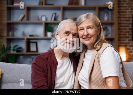 Coppia matura felice sorridendo alla macchina fotografica con un sorriso abbagliante, denti bellissimi. Marito e moglie dai capelli grigi si abbracciano. Relazioni di Foto Stock