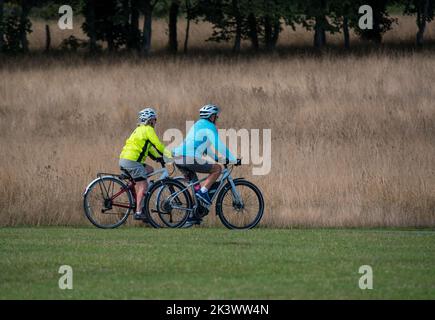 Uomo e donna di mezza età in bicicletta, pedalando sulla pista ciclabile da Bridlington a Sewerby, indossando cime dai colori luminosi e caschi ciclabili Foto Stock