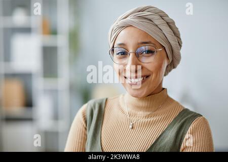 Ritratto minimo di una giovane donna mediorientale sorridente alla fotocamera in ufficio e indossando un copricapo, uno spazio per le copie Foto Stock