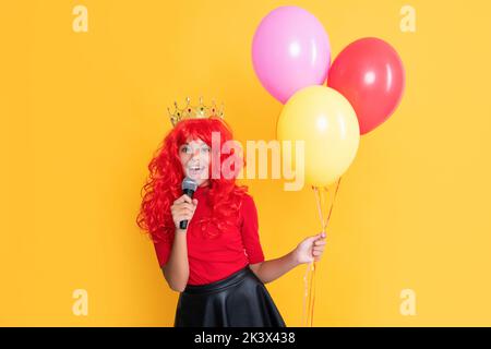 bambino sorridente in corona con microfono e party balloon su sfondo giallo Foto Stock