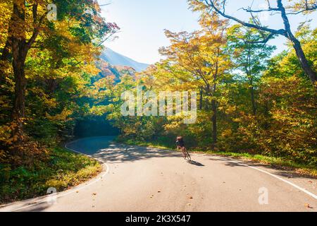 Ciclisti in bicicletta lungo una strada curvilinea a forma di S in una giornata autunnale in Vermont Foto Stock