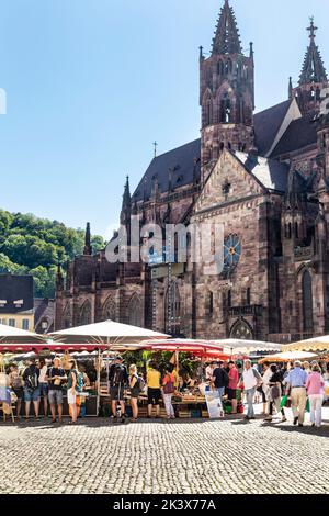 Mercato Münstermarkt affollato sulla Münsterplatz con la cattedrale gotica di Friburgo sullo sfondo, Friburgo in Breisgau, Germania Foto Stock