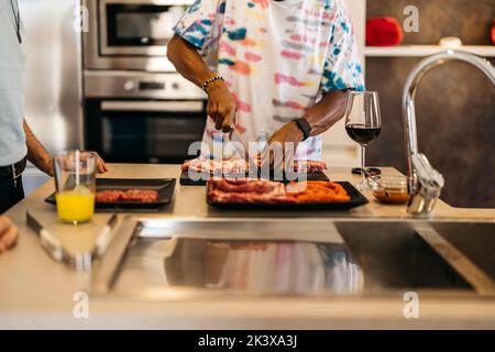 un uomo latino prepara carne alla griglia mentre beve vino rosso Foto Stock