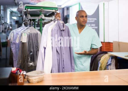 Uomo addetto alla pulitura a secco che dà vestiti al cliente Foto Stock