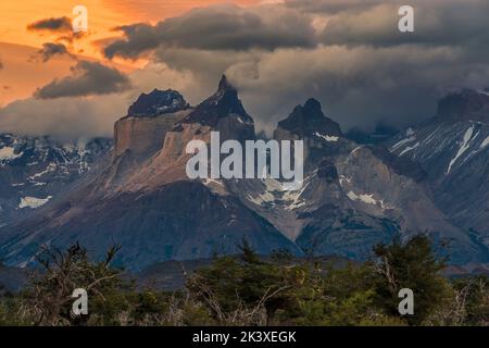 Vista verso nord di Cuernos del Paine (i corni di Paine) al tramonto con una bellissima luce dorata che passa attraverso un'intercapedine in un suggestivo cielo nuvoloso. Torres Foto Stock