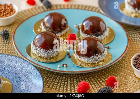 Cupcake con lampone impostato su un piatto blu e decorazioni al cioccolato su un tavolo beige. Dessert alla bacche. Souffle di torta ariosa. Pasticceria appetitosa. Pasta Choux. Foto Stock