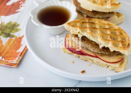 Un sandwich con waffle e salsiccia su un piatto servito con sciroppo d'acero per l'immersione. Foto Stock