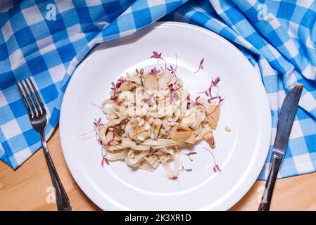 tagliatelle in salsa cremosa con funghi porcini su piatto bianco e tovagliolo bianco e blu a scacchi Foto Stock