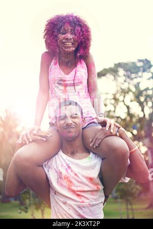 Perché stare in forma quando siete nati per distinguervi. Un giovane uomo che porta una donna sulle sue spalle in una festa di colore. Foto Stock