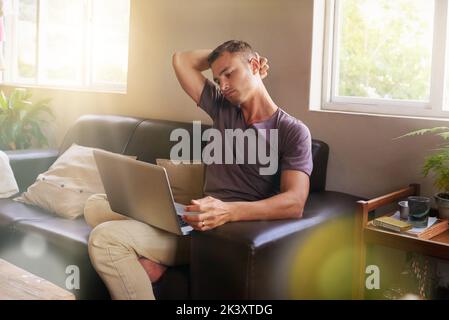 Ci si rilassa con il computer portatile. Un bel giovane che usa un computer portatile sul divano di casa. Foto Stock