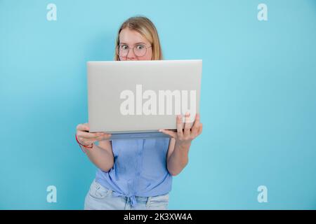 Ritratto di ragazza scioccata adolescente con capelli lunghi indossare camicia blu senza maniche, tenendo il portatile su sfondo blu. Foto Stock