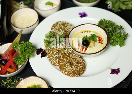 Ciotola di hummus fatta in casa, decorata con ceci bolliti, erbe aromatiche, pita e olio d'oliva su un fondo rustico di metallo