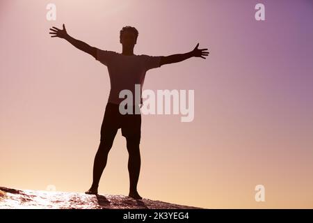 In cima al mondo. Silhouette ripresa da un giovane uomo in piedi contro il cielo. Foto Stock