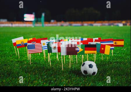 Bandiere nazionali di Qatar, Brasile, Germania, Stati Uniti e altri paesi di calcio sul verde erba di Stadio di notte. Pallone da calcio, sfondo nero Foto Stock