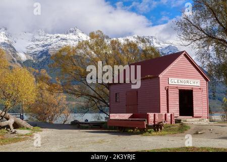 Il vecchio deposito di navi a vapore a Glenorchy, Nuova Zelanda, comunemente noto come "Red Shed", con alberi autunnali e le Humboldt Mountains sullo sfondo Foto Stock