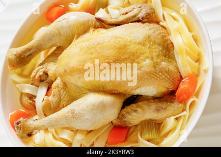 primo piano di zuppa di pollo caldo con pollo intero, pasta, sedano, cipolla e carota in un recipiente bianco Foto Stock