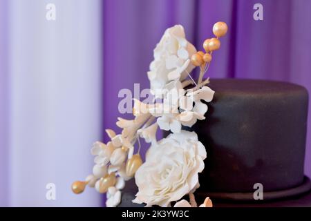 Vista ravvicinata torta nuziale. Bouquet di fiori beige su torta con marzapane nero Foto Stock