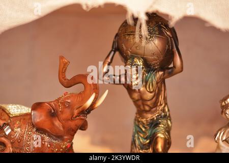 Statua di bronzo con un uomo che porta dietro il globo della terra e un elefante di legno visto in profilo. L'uomo è Atlas Foto Stock