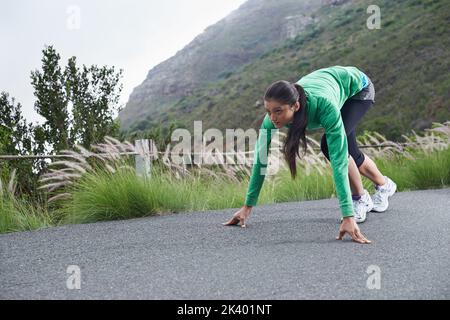 Pronto a rendere questa strada sua... Una giovane donna accovacciata sulla strada che sta per andare per una corsa. Foto Stock