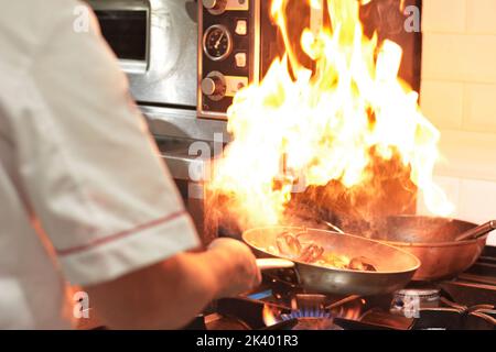 Chef che cucina con fiamma. Cucina del ristorante. Albergo. Foto Stock