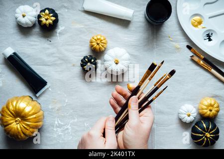 Dipingere con le mani femminili zucche nere e dorate. Idee creative di pittura della zucca per Halloween e il Ringraziamento per gli adulti. Semplice zucca facile Foto Stock