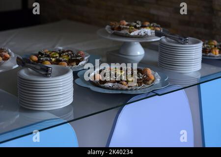 Più torte sciroppose sul tavolo di vetro e pile di piatti bianchi Foto Stock