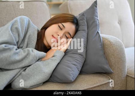 Giovane asiatica rilassata prendendo un pisolino pomeridiano sul divano, dormendo, addormentandosi sul suo comodo divano nel soggiorno. Foto Stock