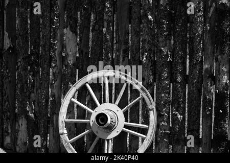 Una vecchia ruota di carro arrugginita appoggiata su una parete di fienile in bianco e nero stock foto Foto Stock