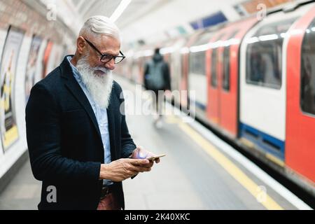 Hippster Senior man telefono cellulare mentre attende per il treno della metropolitana - Focus sulla mano sinistra Foto Stock