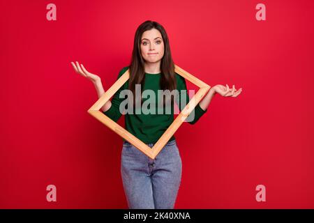 Foto di bruna sconosciuta giovane donna shrug spalle in cornice indossare camicia verde isolato su sfondo di colore rosso Foto Stock