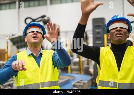 Ingegneri multietnici che utilizzano futuristici occhiali per realtà aumentata all'interno di una fabbrica robotica - concentrati sul volto dell'uomo sinistro Foto Stock