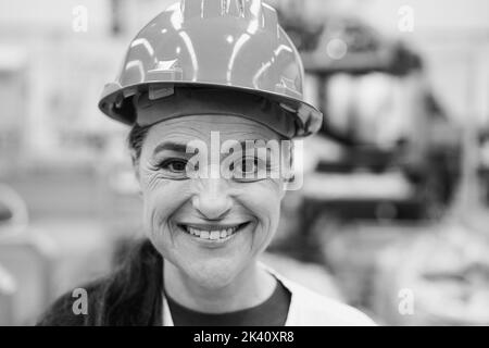 Ingegnere senior donna che lavora all'interno di una fabbrica robotica - Focus su hardhat - montaggio in bianco e nero Foto Stock