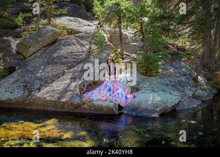 Bella giovane brunetta seduta sulle rocce vicino ad un fiume Foto Stock