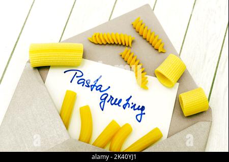 busta con testo di auguri di pasta e vari tipi di pasta cruda cruda cruda su sfondo di legno bianco come conceptof grafico pasta alimentare Foto Stock