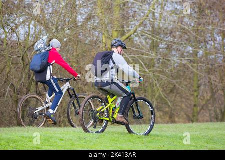 Vista laterale di due ciclisti in mountain bike con zaini in bicicletta sull'erba nel parco di campagna, Regno Unito. Foto Stock