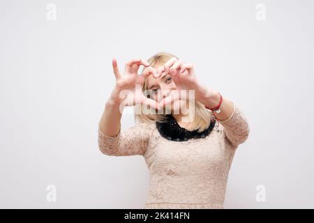 Donna che mostra mani cuore su uno sfondo bianco Foto Stock