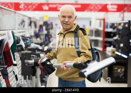 Uomo anziano che sceglie la felpa con cappuccio verticale nello showroom del negozio di elettrodomestici Foto Stock