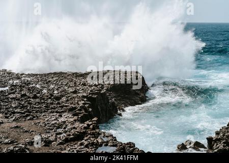 Spruzzi d'acqua sulle rocce vulcaniche nere di Tenesar, Lanzarote, Isole Canarie, Spagna Foto Stock