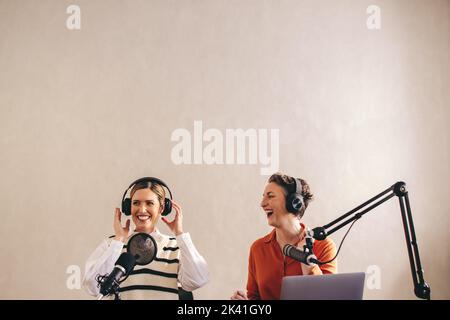 Presentatori radio femminili ridendo e avendo un buon tempo mentre co-ospitando una trasmissione audio dal vivo. Due donne felici che registrano una serie di podcast dal vivo su thei Foto Stock