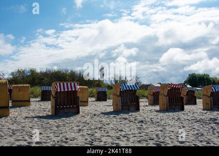 Vista sulle tradizionali sedie a sdraio marroni in vimini e sul faro sulla spiaggia sabbiosa del Mar Baltico, vicino a Timmendorf Strand, sull'isola Foto Stock