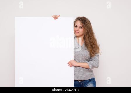 Bella donna che posa dietro un pannello bianco isolato su sfondo bianco foto stock Foto Stock
