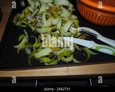 Bucce di frutti di pera sbucciate durante il processo di conservazione della pera. Le bucce sono posizionate su un vassoio di metallo con un coltello e una pelatrice accanto ad esso Foto Stock