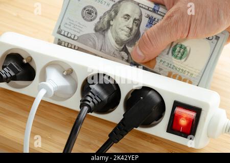 Aumenti dei prezzi dell'elettricità negli Stati Uniti, Energy Concept, Power Strip con spine collegate e un grande pacchetto di dollari in mano, increas Foto Stock