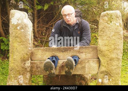 Un uomo 60+ che guarda miserabile seduto con i suoi piedi nelle scorte del villaggio Foto Stock