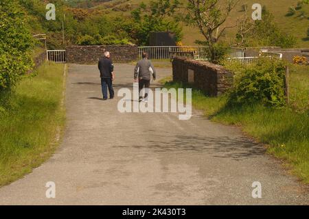 Due uomini 60+ camminando lungo una strada vicino a Meldon Dam, Devon, Inghilterra, godendosi il sole primaverile Foto Stock