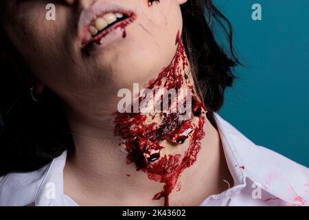 Mostro di Halloween con ferite sanguinose sul collo, in posa in studio su sfondo blu. Zombie irreale mangiare cervello e ferirsi, avendo brutto sporche cicatrici e graffi con il sangue. Primo piano. Foto Stock