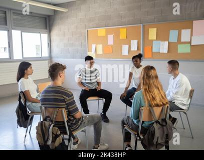 Gruppo di studenti multietnici che si siedono in cerchio in classe mentre parlano delle loro emozioni. Educazione emotiva, assemblea, scuola superiore Foto Stock